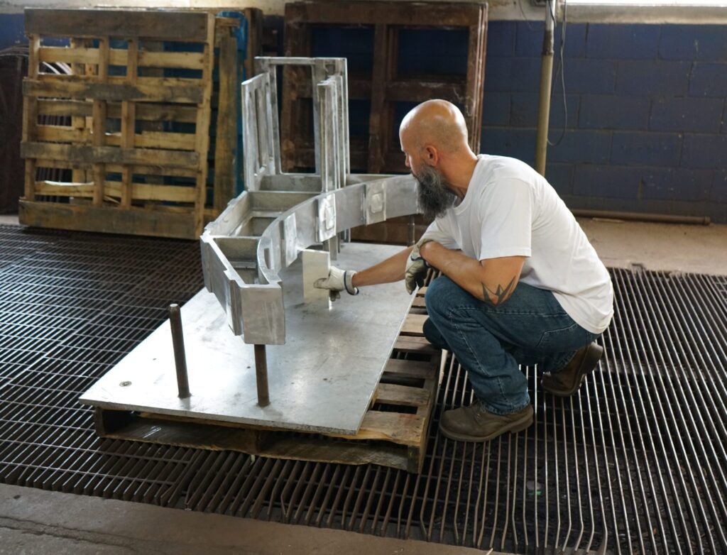 A man crouched down working on an aluminum part.