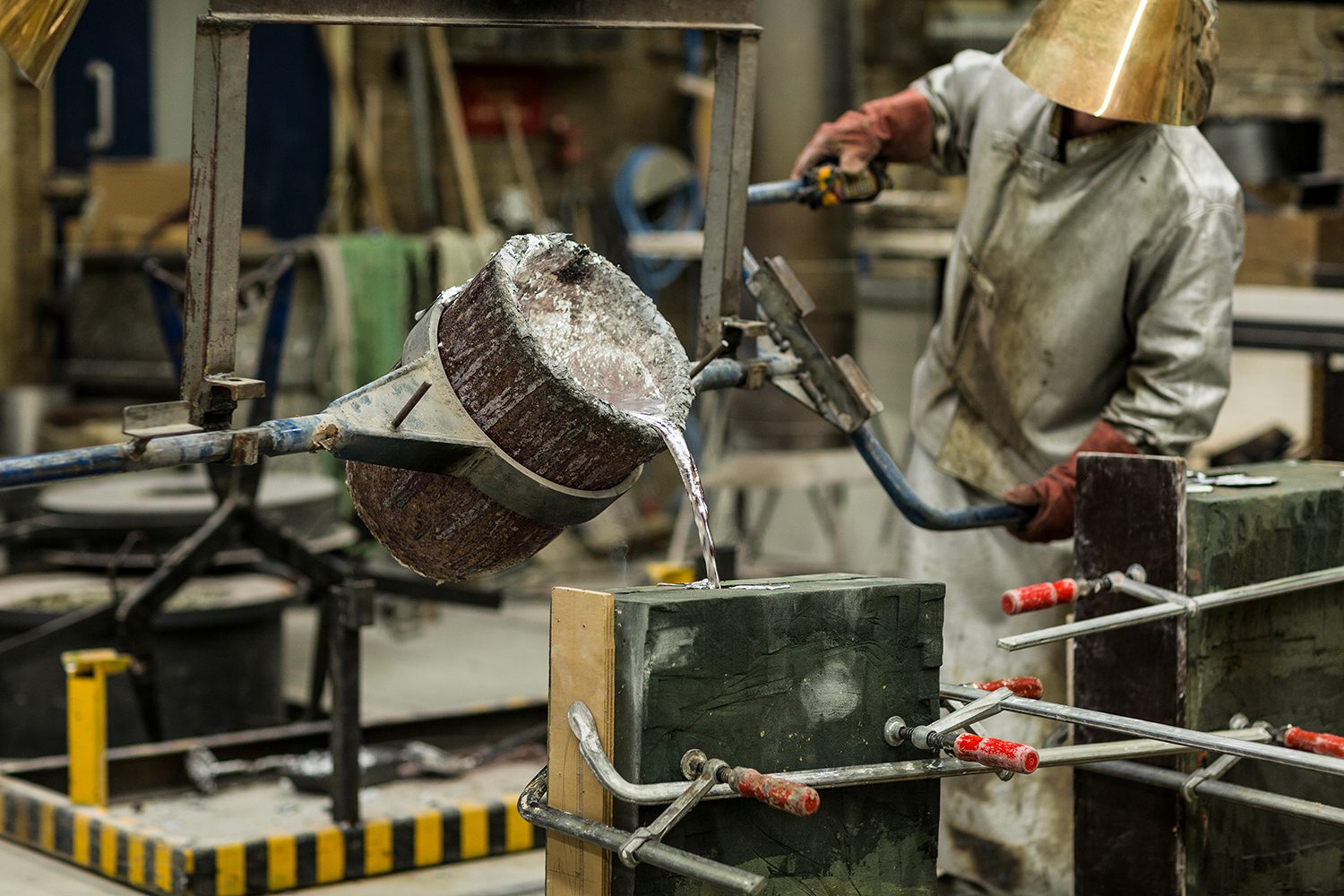 Craftsmen pouring molten aluminum into sand casting mold in workshop.